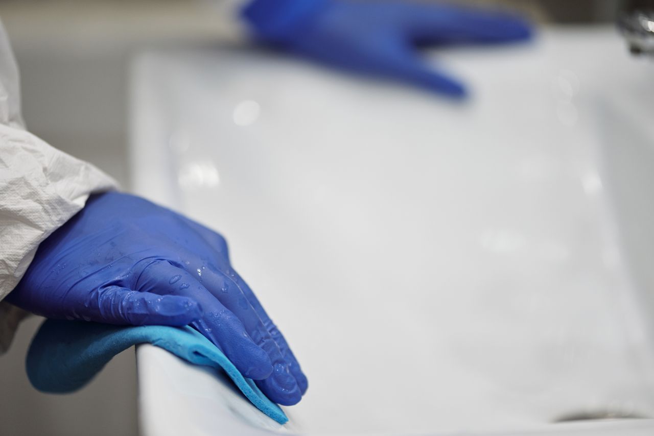 services-03 Gros plan d’une personne nettoyant un lavabo de salle de bain avec des gants et un chiffon, dans une mise en avant de l’hygiène et de la propreté.