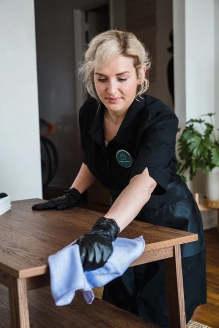 who-we-are A person in full protective gear disinfecting a leather couch indoors with careful attention to hygiene and safety.